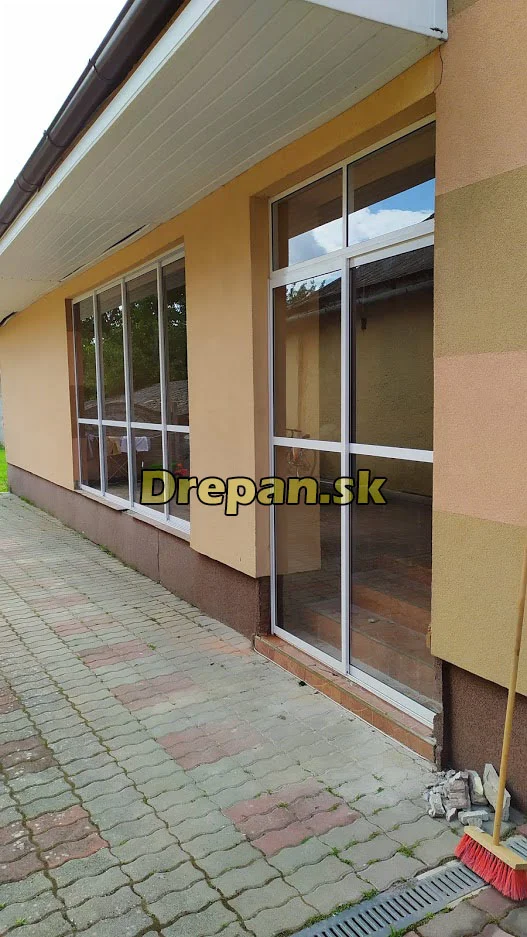 Zasklenie pozdĺžnej terasy hliníkovým rámom s posuvnými sklenenými krídlami a presklenými dverami pozdĺž zámkovej dlažby Zasklenie pozdĺžnej terasy hliníkovým rámom s posuvnými sklenenými krídlami a presklenými dverami pozdĺž zámkovej dlažby, projekt 13, DREPAN, východné a stredné Slovensko